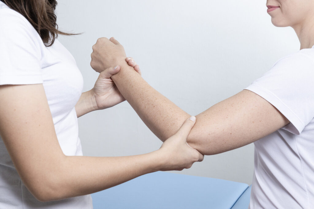 Doctor physiotherapist assisting a woman patient while giving exercising treatment massaging the arm of patient in a physio room. Rehabilitation physiotherapy concept.